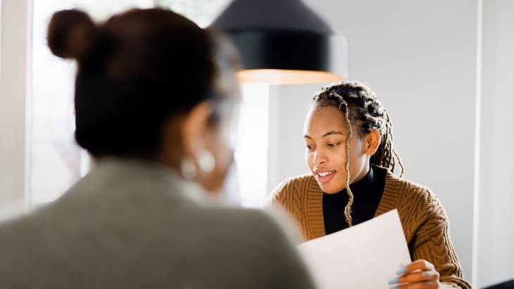 Alt - Female candidate giving her resume to HR manager during a job interview in office