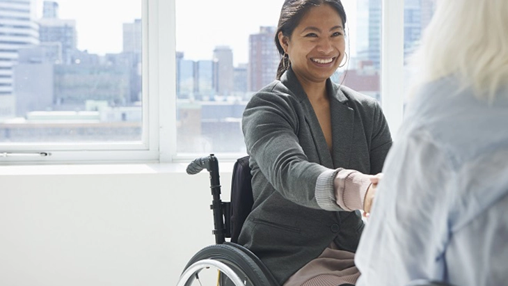 Smiling woman in wheelchair shaking hands with another person