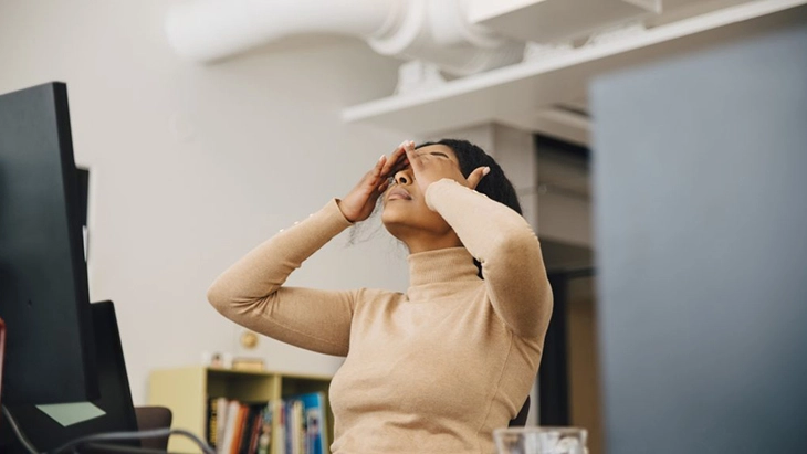 Woman working at desk and covering eyes with her hands