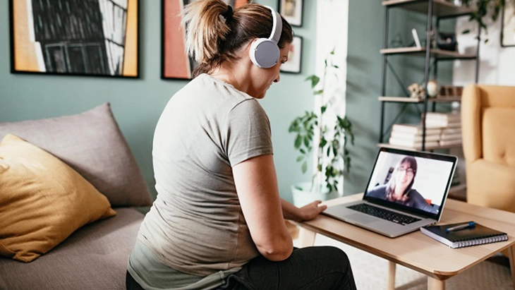 Woman wearing headphone working on laptop in living room