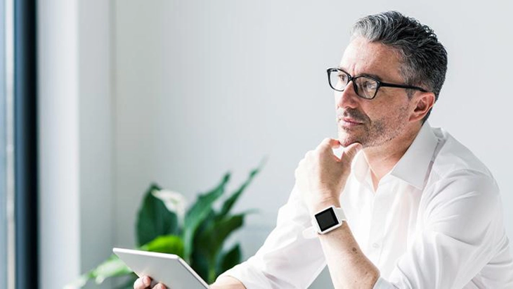 Alt - A man in glasses using a tablet on a desk, thinking.