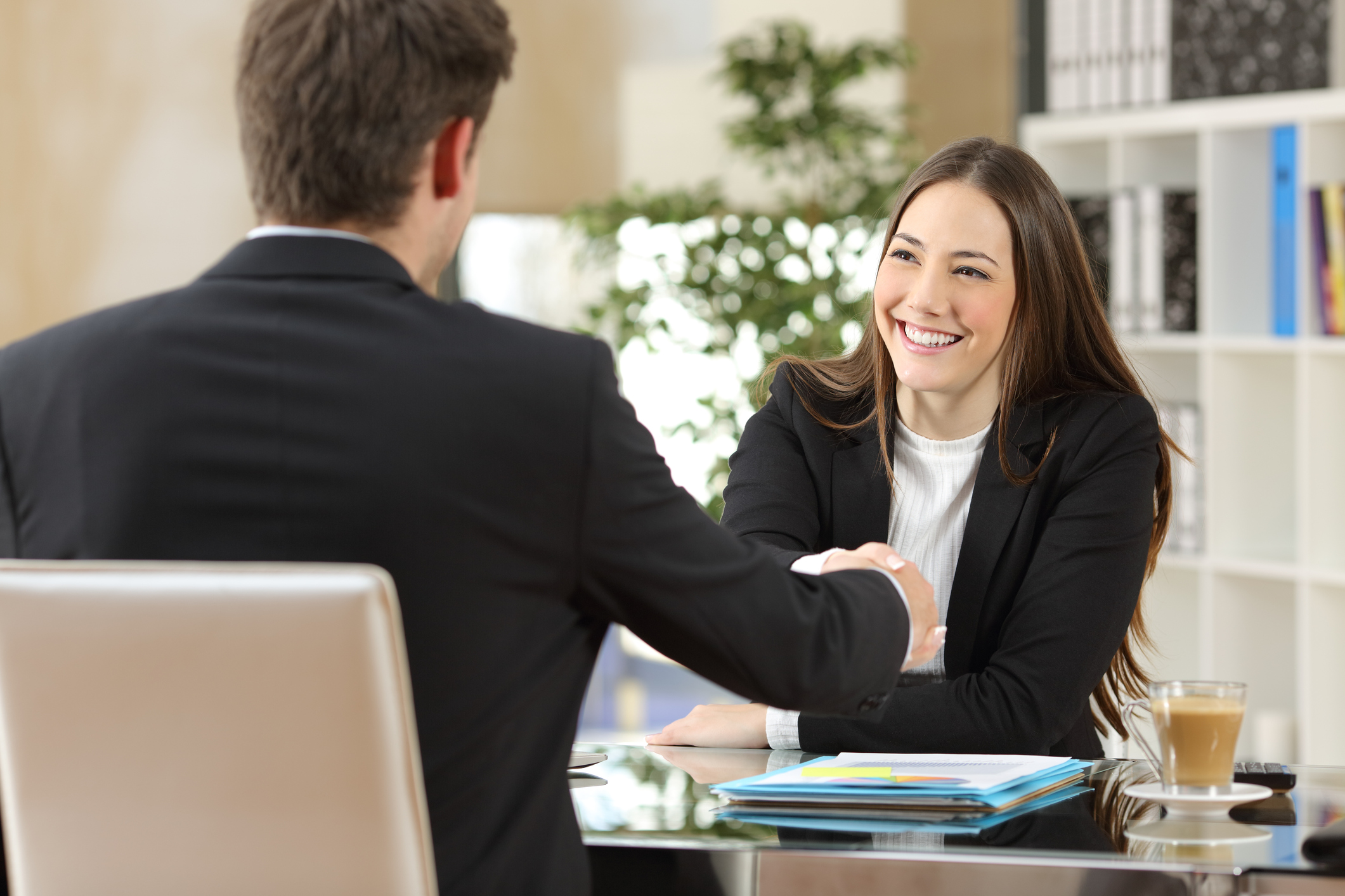 Alt - Two professionals, one man, and one woman shaking hands in an office.